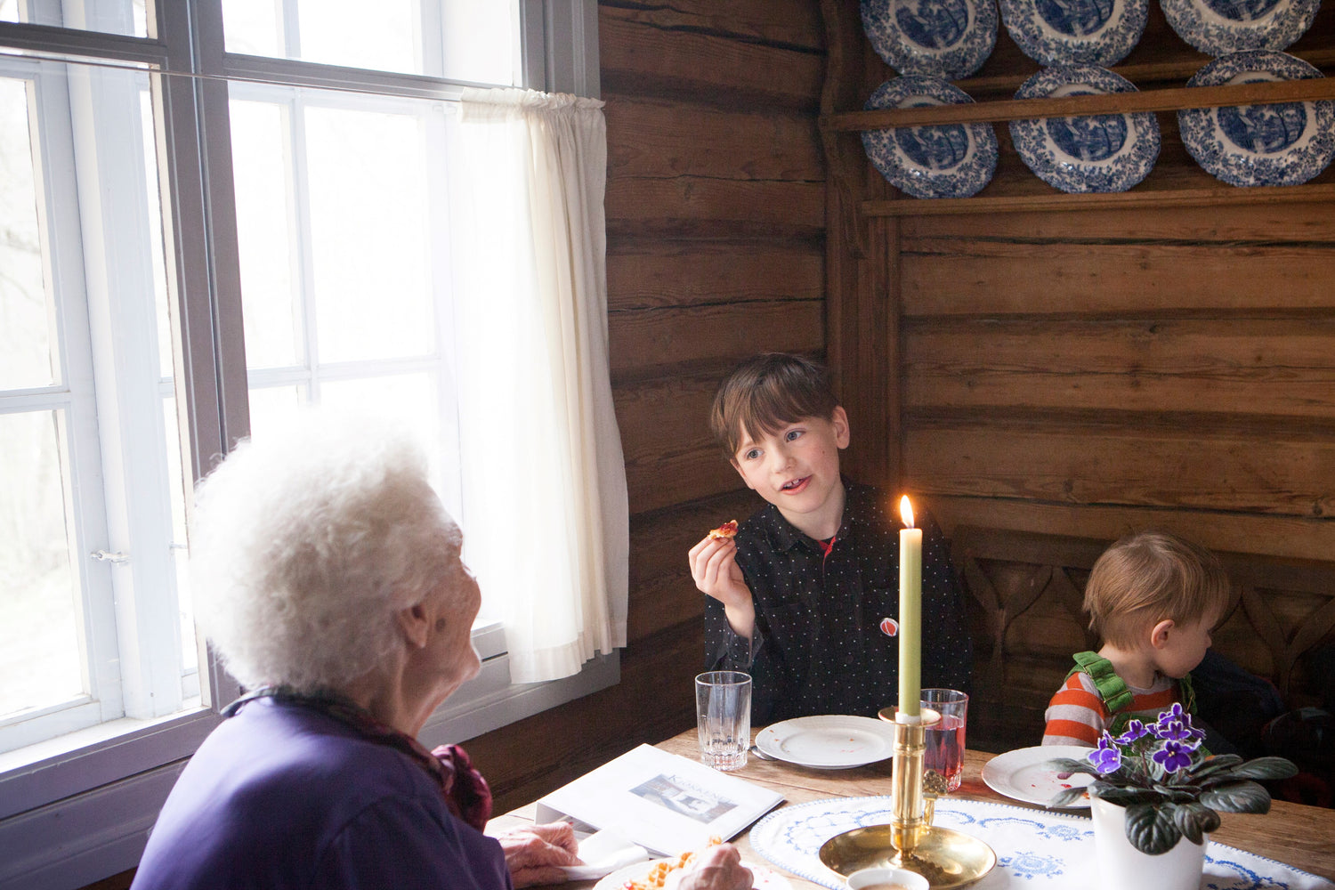 Eldre kvinne snakker med to barn på kafé.