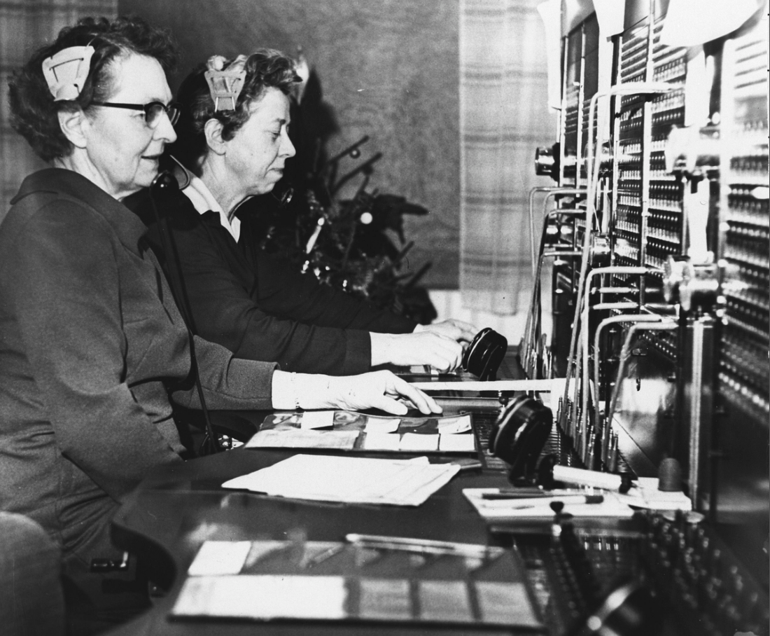 To kvinnelige telefonister sitter ved sentralbord.