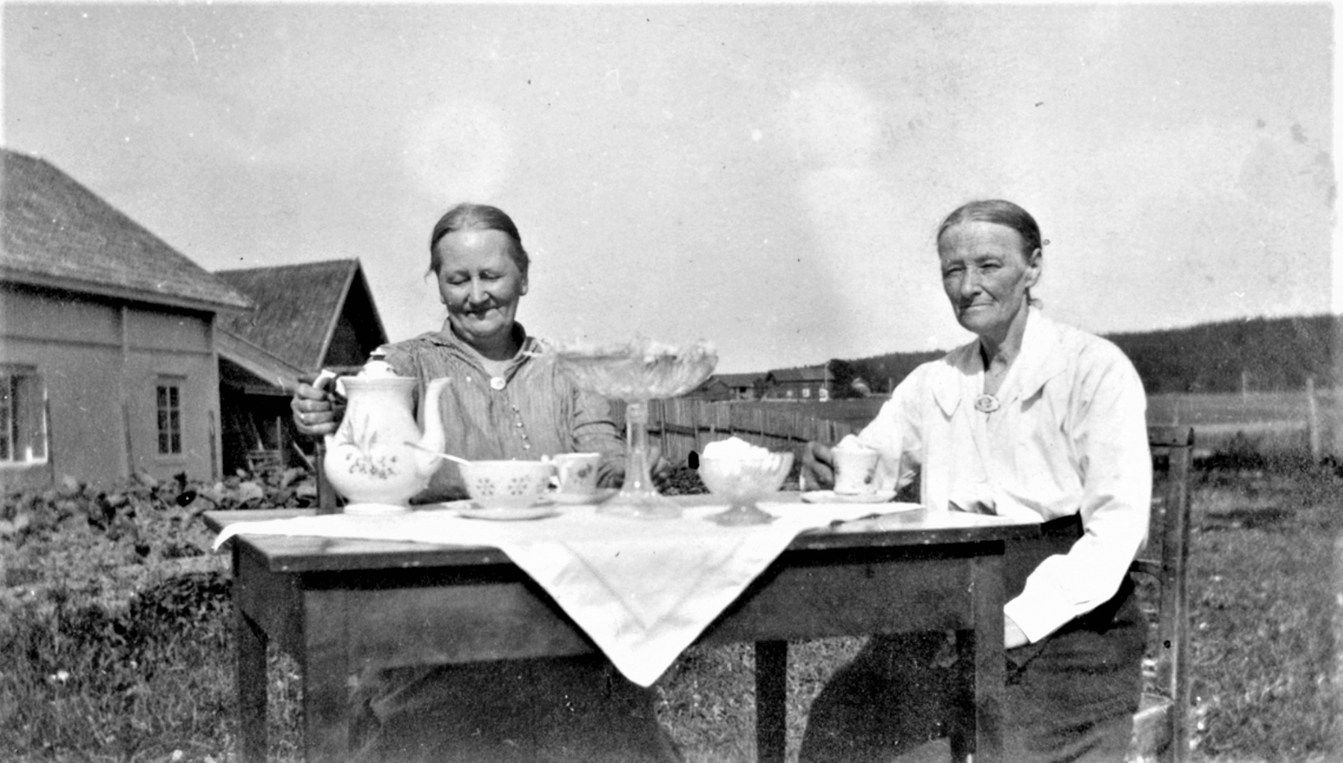 To damer drikker kaffe ved et bord.